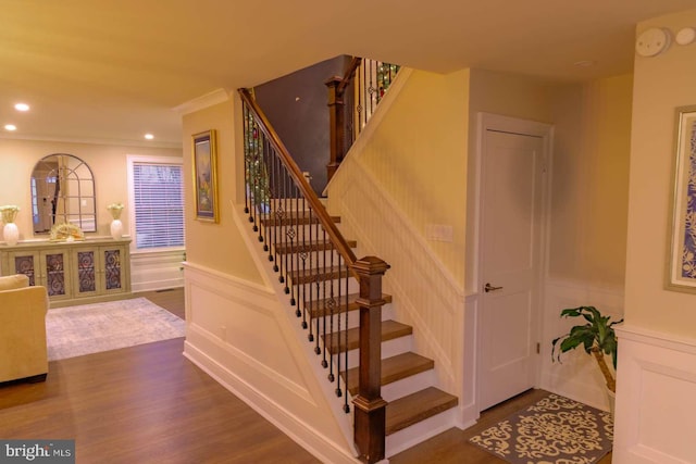 stairway with a wainscoted wall, wood finished floors, crown molding, a decorative wall, and recessed lighting