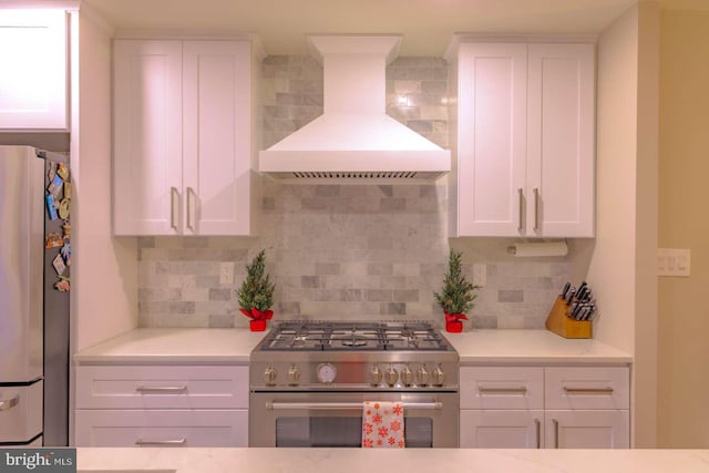 kitchen with high end stainless steel range, decorative backsplash, freestanding refrigerator, white cabinetry, and premium range hood