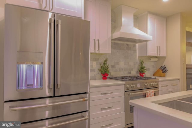 kitchen featuring wall chimney range hood, white cabinetry, stainless steel appliances, and backsplash