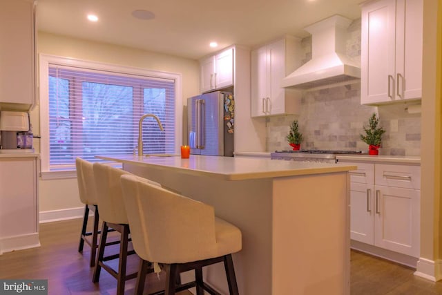 kitchen featuring a center island with sink, light countertops, custom range hood, appliances with stainless steel finishes, and white cabinetry