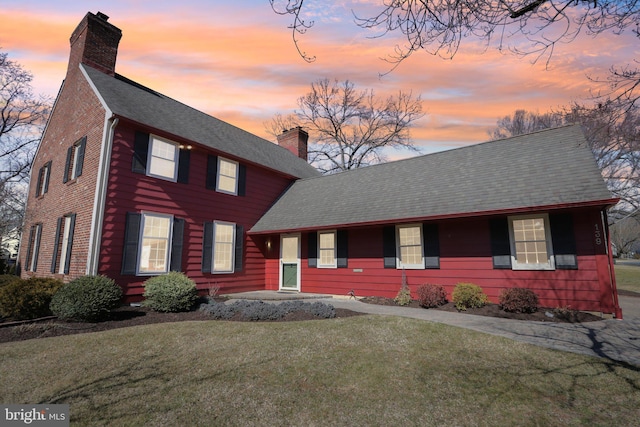 view of front of home featuring a shingled roof, a front yard, and a chimney