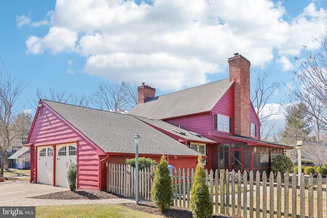 view of front facade featuring a fenced front yard, a chimney, a shingled roof, and concrete driveway