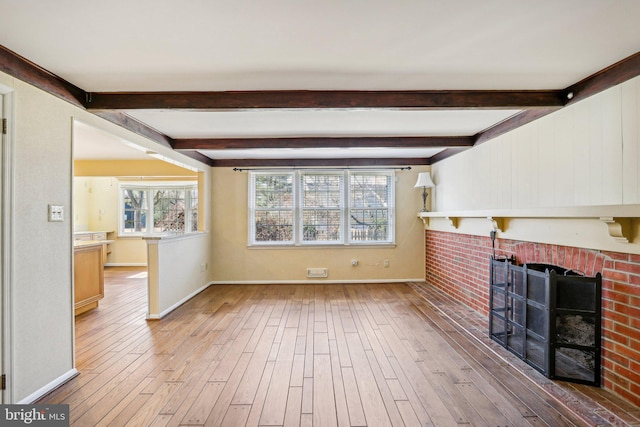 unfurnished living room with a brick fireplace, baseboards, wood finished floors, and beamed ceiling