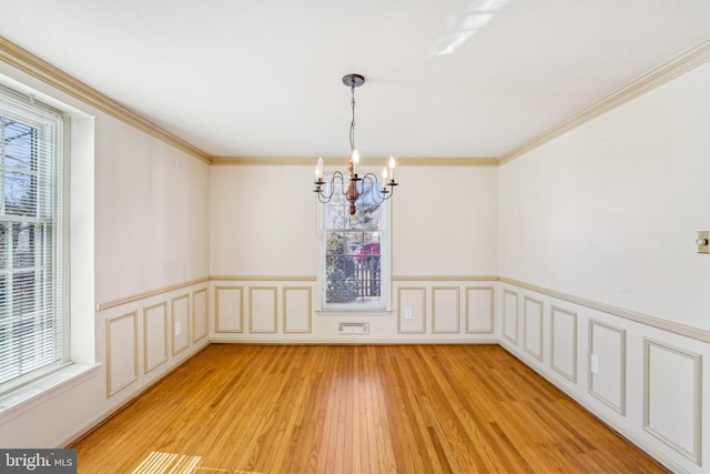 unfurnished dining area with a healthy amount of sunlight, crown molding, a notable chandelier, and light wood finished floors