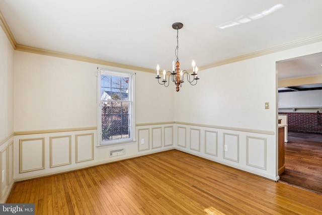 empty room with crown molding, a wainscoted wall, a chandelier, and light wood-style floors