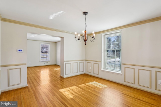 unfurnished dining area with a decorative wall, crown molding, light wood-style floors, wainscoting, and an inviting chandelier