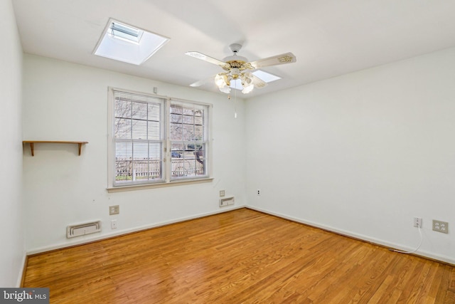 spare room with ceiling fan, a skylight, wood finished floors, visible vents, and baseboards