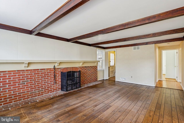 unfurnished living room with visible vents, a fireplace, beamed ceiling, and hardwood / wood-style floors