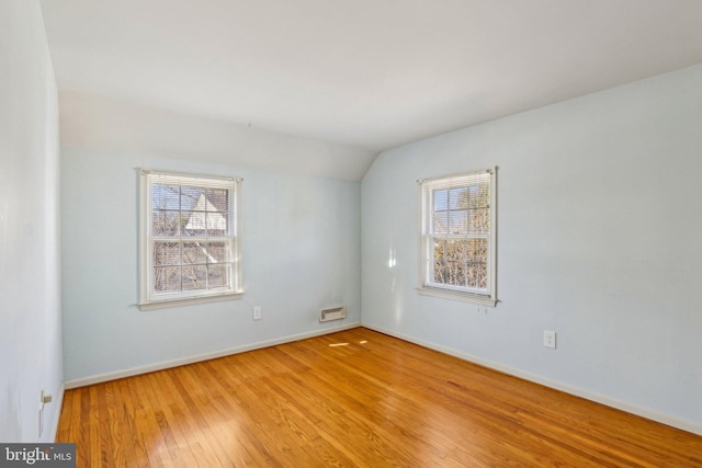 spare room with vaulted ceiling, wood-type flooring, and baseboards