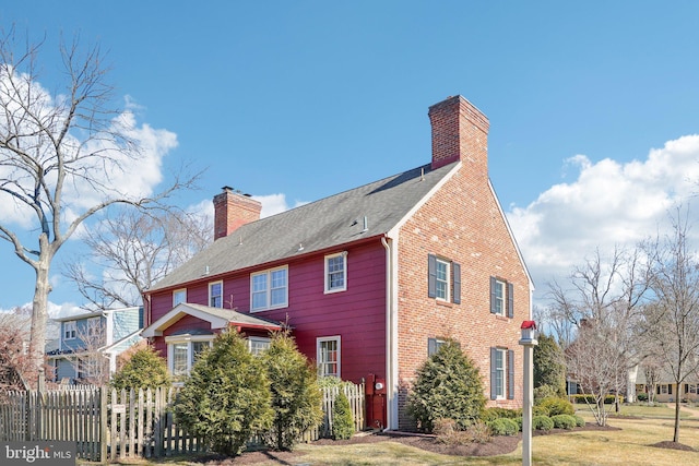 exterior space featuring roof with shingles, a chimney, fence, and a lawn