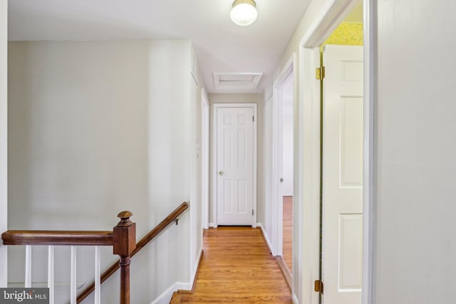 hallway featuring attic access, an upstairs landing, light wood-style flooring, and baseboards