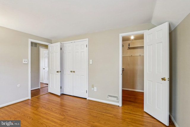 unfurnished bedroom featuring visible vents, vaulted ceiling, baseboards, and wood finished floors