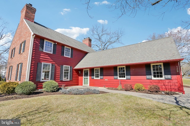 view of front facade featuring a shingled roof, a chimney, and a front yard