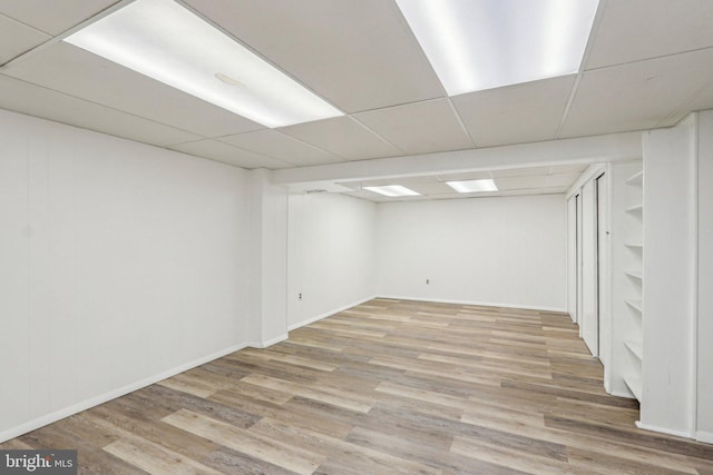 finished basement with a paneled ceiling, baseboards, and wood finished floors