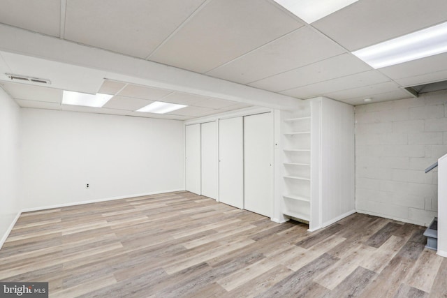 finished below grade area featuring concrete block wall, baseboards, visible vents, a drop ceiling, and wood finished floors