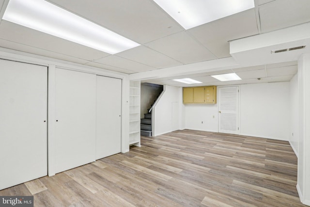 finished below grade area featuring stairs, visible vents, light wood-type flooring, and a paneled ceiling