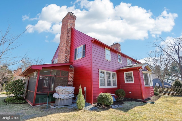 view of side of property with a yard, a chimney, fence, and a sunroom