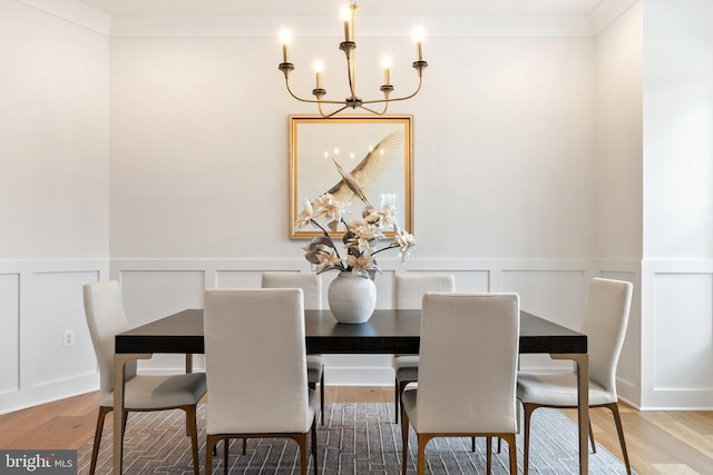 dining area featuring crown molding, a decorative wall, wood finished floors, and a notable chandelier