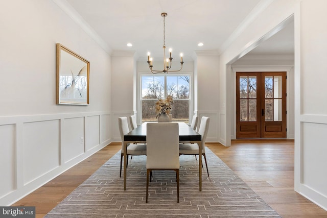 dining space featuring an inviting chandelier, crown molding, a decorative wall, and wood finished floors