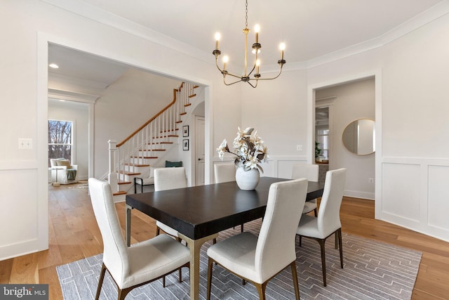 dining space with stairs, a decorative wall, crown molding, and light wood-style floors