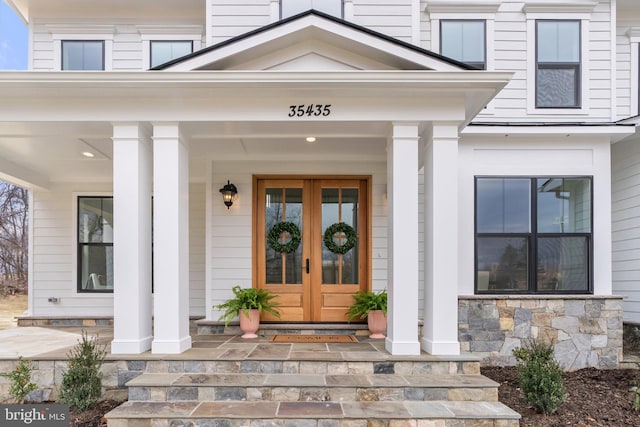 view of exterior entry featuring french doors, a porch, and stone siding