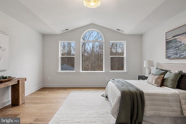 bedroom featuring light wood finished floors, baseboards, visible vents, and vaulted ceiling