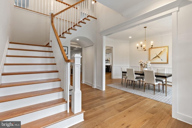 stairs featuring arched walkways, a decorative wall, ornamental molding, wood finished floors, and a chandelier