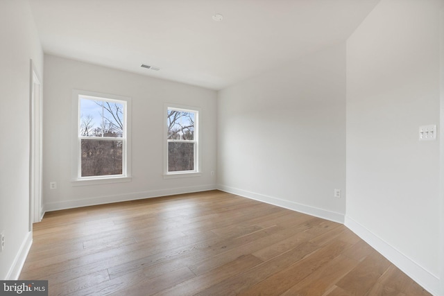 spare room featuring light wood-type flooring, visible vents, and baseboards