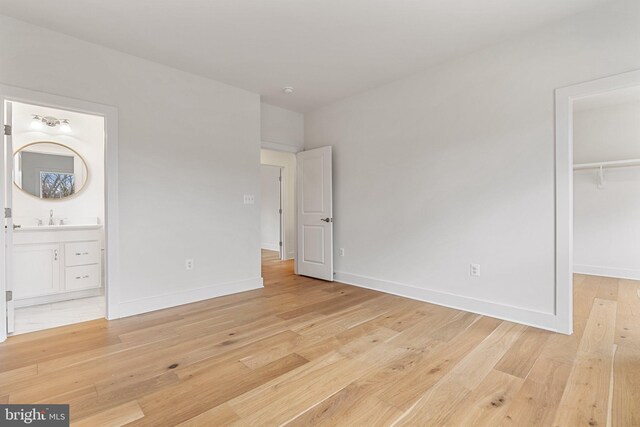 unfurnished bedroom featuring a closet, baseboards, a walk in closet, light wood-style floors, and a sink