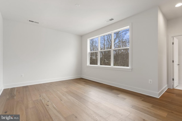 spare room featuring wood-type flooring, visible vents, and baseboards