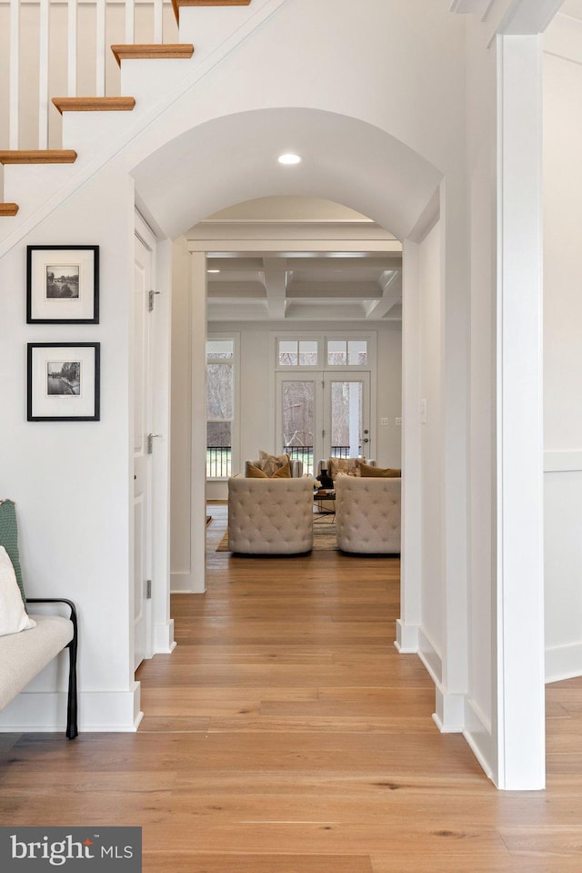 hallway with light wood-type flooring, baseboards, arched walkways, and coffered ceiling