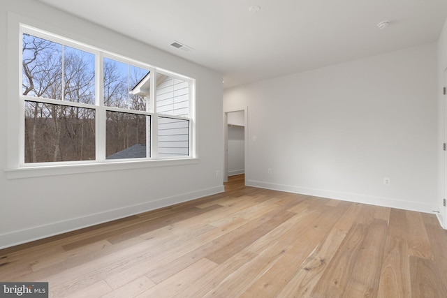 empty room featuring light wood-type flooring, visible vents, and baseboards