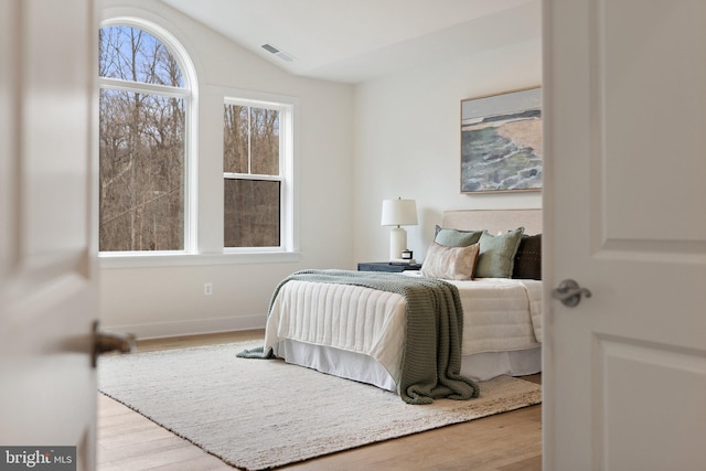 bedroom with lofted ceiling, wood finished floors, visible vents, and baseboards