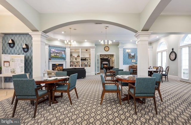 dining area with crown molding, decorative columns, a lit fireplace, and baseboards