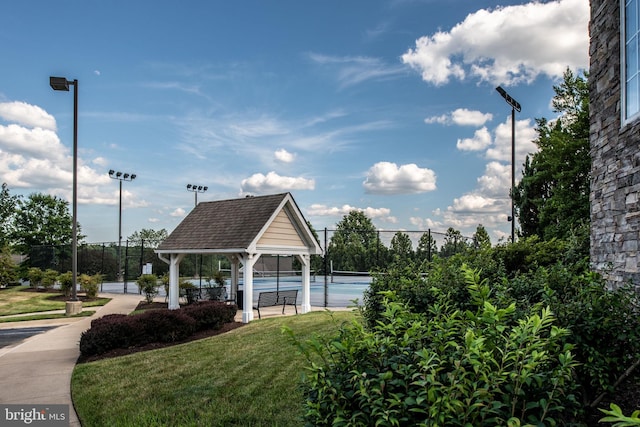 surrounding community featuring a tennis court, fence, and a yard