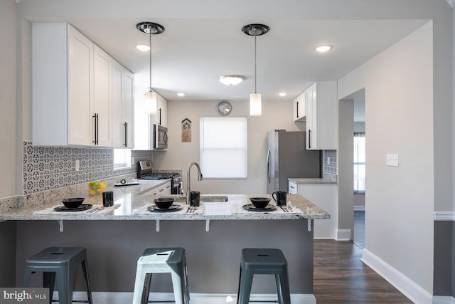 kitchen featuring light stone countertops, a peninsula, a sink, white cabinets, and appliances with stainless steel finishes