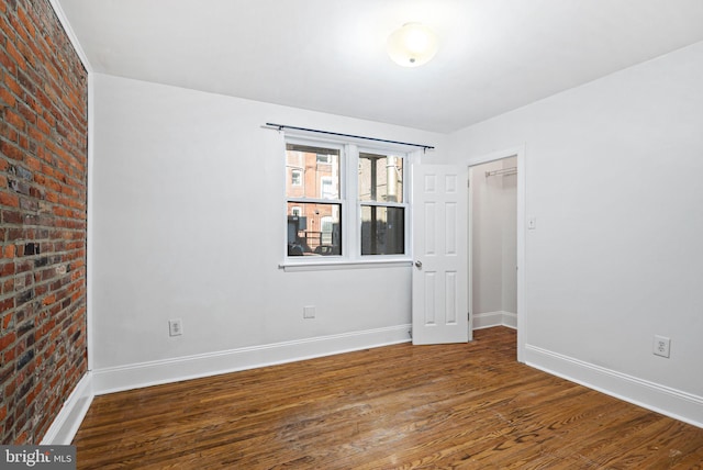 unfurnished room featuring brick wall, baseboards, and wood finished floors