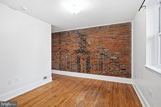 spare room featuring brick wall, baseboards, and wood finished floors