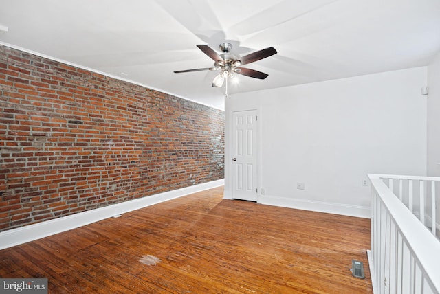 spare room featuring visible vents, ceiling fan, brick wall, baseboards, and hardwood / wood-style flooring