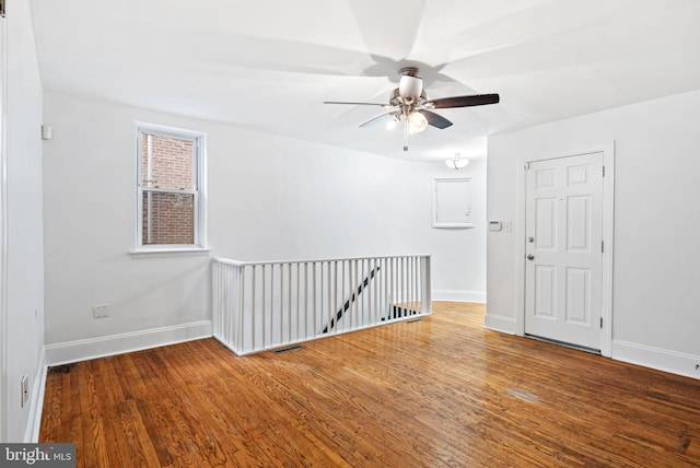 unfurnished room with a ceiling fan, visible vents, baseboards, and wood finished floors