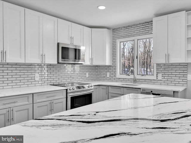 kitchen with a sink, appliances with stainless steel finishes, backsplash, light stone countertops, and open shelves