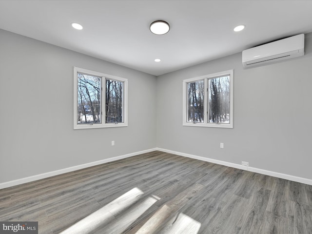 unfurnished room featuring a healthy amount of sunlight, baseboards, an AC wall unit, and wood finished floors