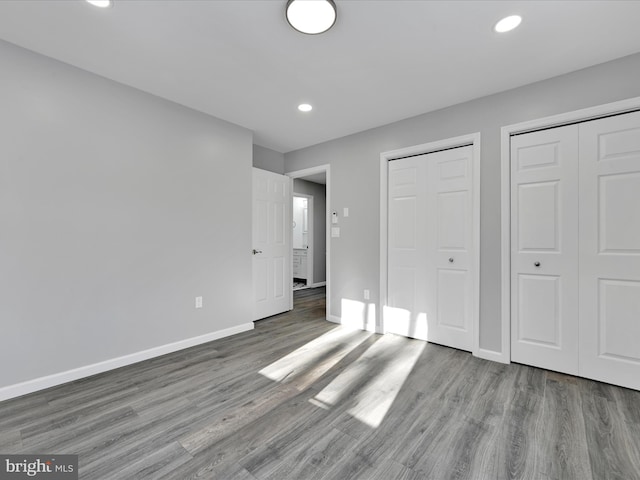 unfurnished bedroom with multiple closets, baseboards, and wood finished floors