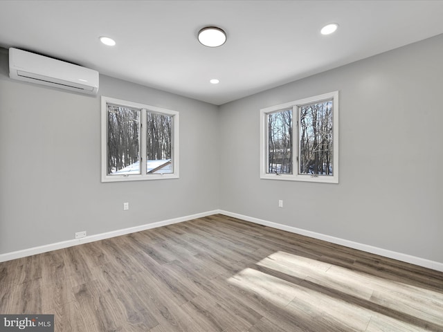 unfurnished room with recessed lighting, an AC wall unit, baseboards, and wood finished floors