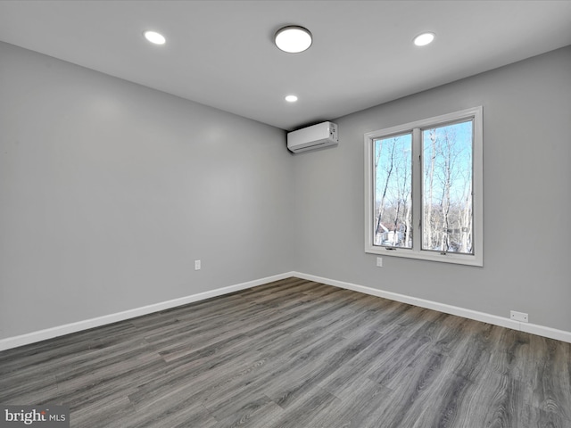 empty room with recessed lighting, a wall unit AC, baseboards, and wood finished floors