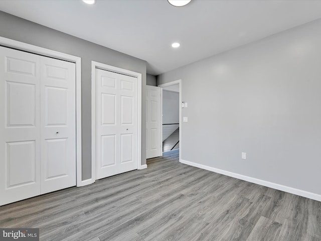 unfurnished bedroom featuring recessed lighting, wood finished floors, baseboards, and two closets