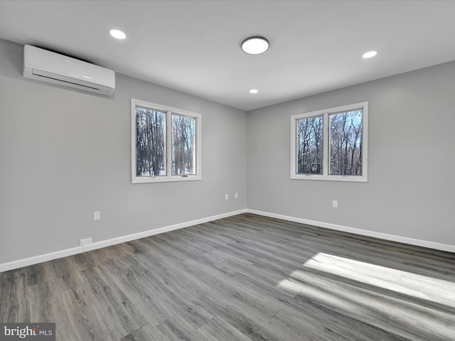 spare room featuring an AC wall unit, a healthy amount of sunlight, baseboards, and wood finished floors