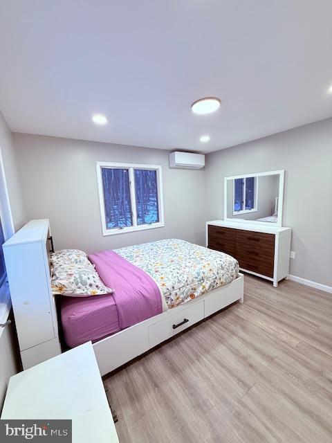 bedroom featuring light wood-type flooring, a wall unit AC, baseboards, and recessed lighting