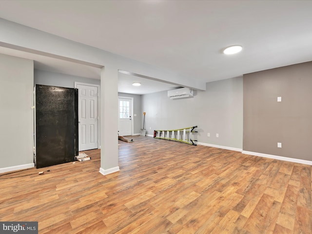 basement with a wall unit AC, light wood-style flooring, and baseboards