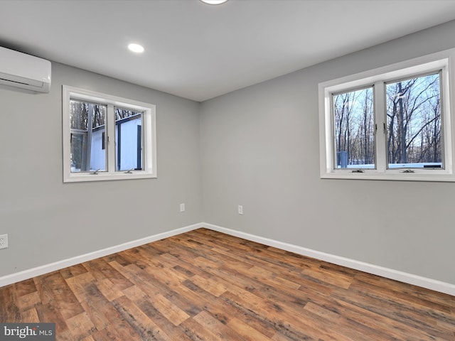 unfurnished bedroom with recessed lighting, a wall unit AC, baseboards, and wood finished floors